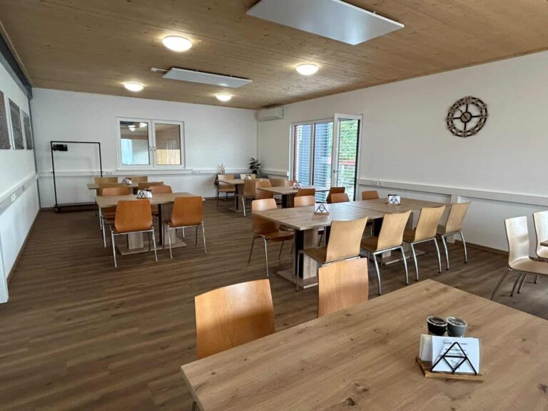 Kantinenbereich für Mitarbeitende im Kompetenzzentrum von TC Maschinenbau mit Holztischen, Stühlen und großen Fenstern.